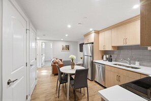 A modern kitchen with wooden cabinets, stainless steel appliances, and a dining area with a white table and chairs. - Luxury 2bedroom Suite With Park Views in Calgary (Calgary)