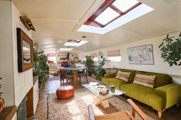 A spacious living area with a green sofa, a glass coffee table, and a dining area with a table and chairs.