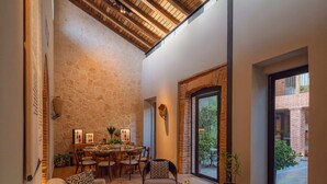 A modern interior with a wooden ceiling, a stone wall, a dining area, and a large window. - Casa del Orfebre Colonial Home in Zona Colonial , Pool & Private Patio (Santo Domingo)