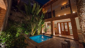 A pool area with a brick patio, surrounded by lush greenery and a wooden deck. - Casa del Orfebre Colonial Home in Zona Colonial , Pool & Private Patio (Santo Domingo)