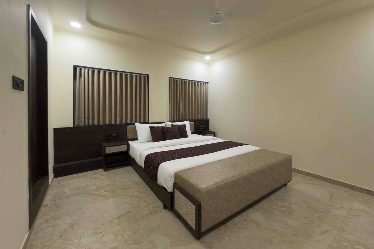 Una habitación de hotel con una cama, mesitas de noche, un ventilador de techo y un ventanal con persianas.