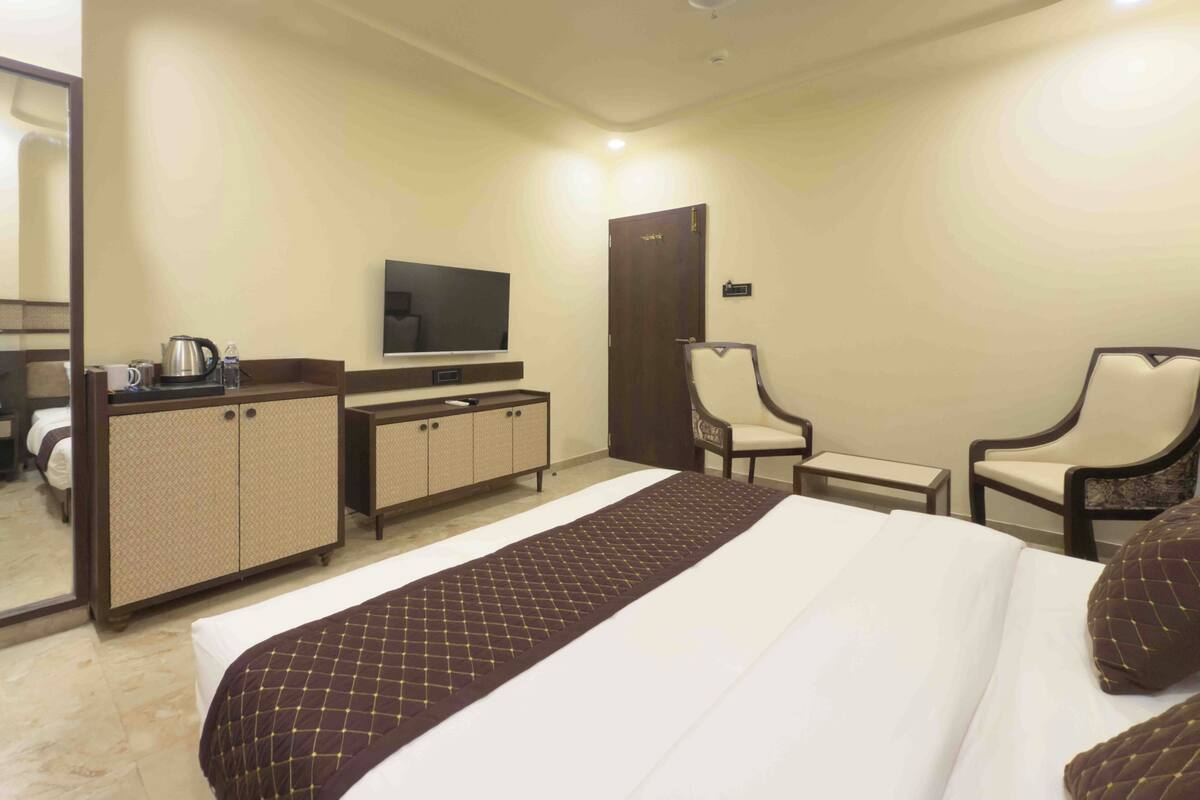 Habitación de hotel con cama, televisor, escritorio, dos sillas, armario y espejo.