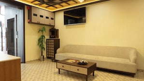 A living room with a sofa, a coffee table, a TV, a cabinet, and a plant. - Hotel Liora (Rajkot)