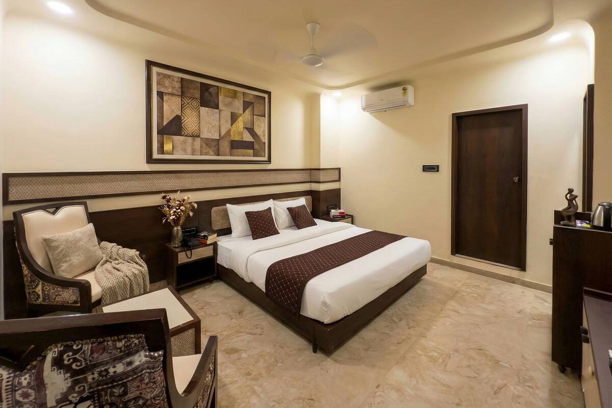 Habitación de hotel con una cama grande, una silla, una mesita de noche, un equipo de aire acondicionado y una puerta.