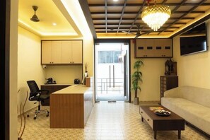 Un salon moderne comprenant un canapé, une table basse, un bureau avec une chaise, un téléviseur fixé au mur et un ventilateur de plafond.