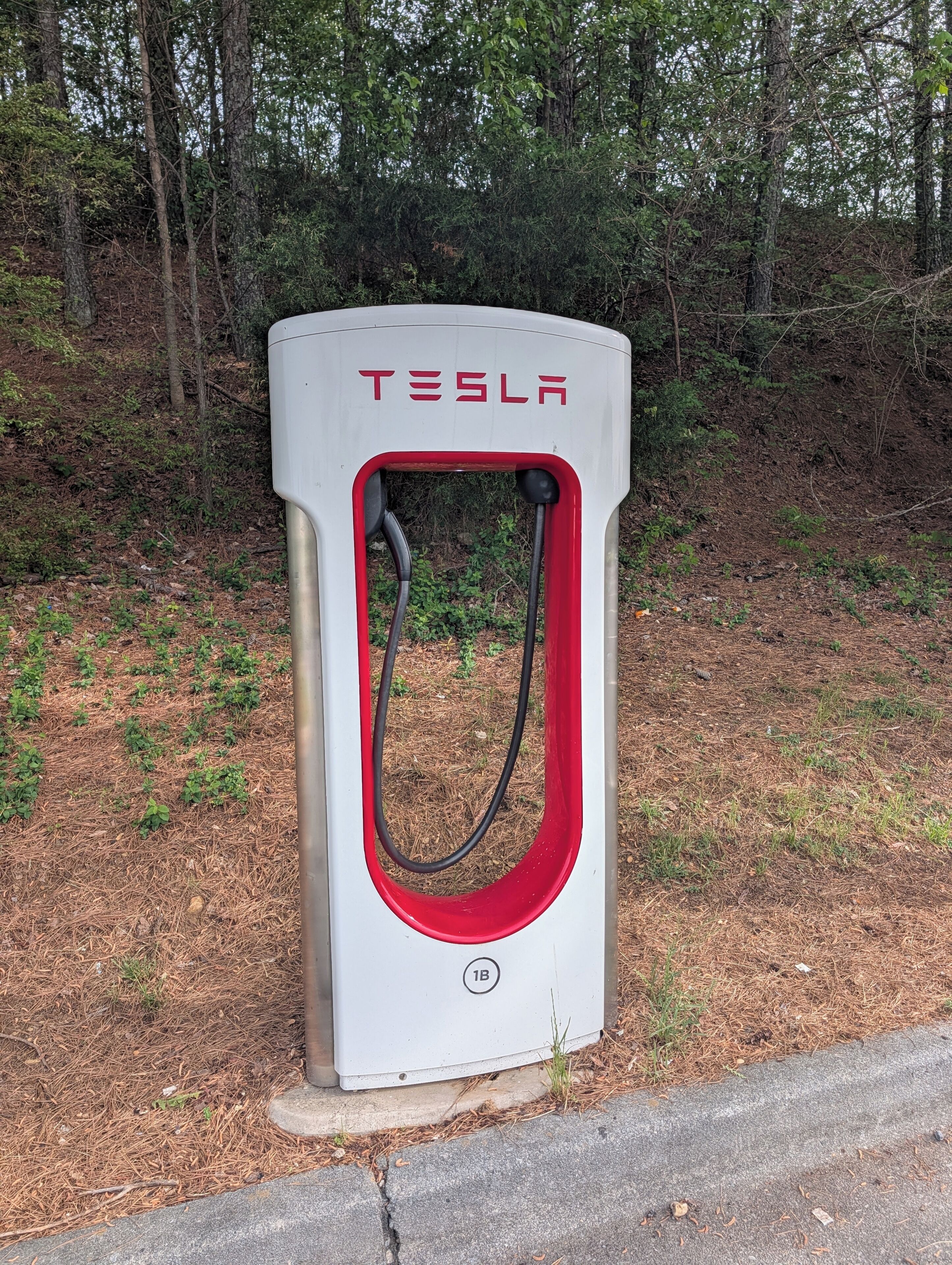A Tesla electric vehicle charging station with a red and white design, surrounded by a wooded area.