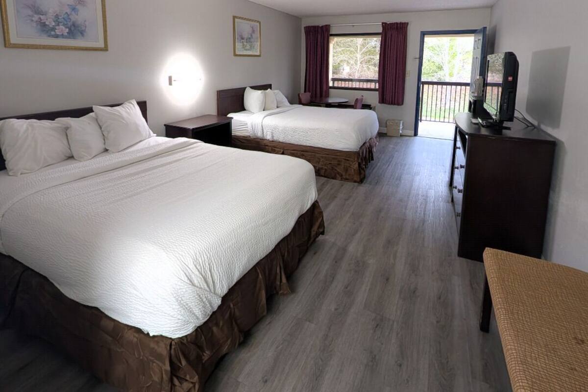 Habitación de hotel con dos camas, un escritorio, un televisor y una ventana con cortinas.