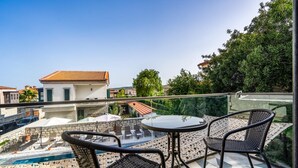 Un balcón con una mesa y sillas de vidrio, una piscina y vistas a edificios y árboles.