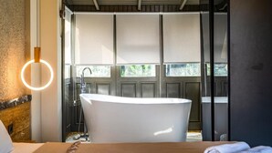 Un baño con una bañera independiente, una lámpara moderna y vistas a través de una puerta.