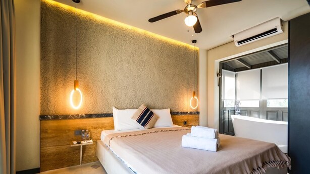 Habitación de hotel con cama, ventilador de techo, aire acondicionado y vista al exterior.