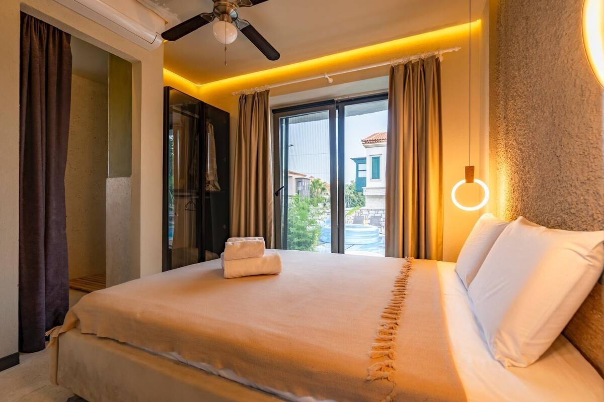 A hotel room with a bed, a ceiling fan, a window with curtains, and a view of the outside.