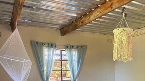 Una habitación con una cama, mosquitero colgante, ventilador e lámpara de techo tejida.