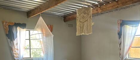 A room with a bed, a small table, a fan, and a hanging decorative piece.