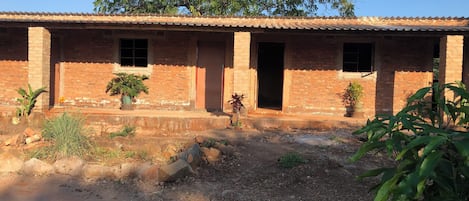 A brick building with multiple doors and windows, surrounded by a gravel area with potted plants.