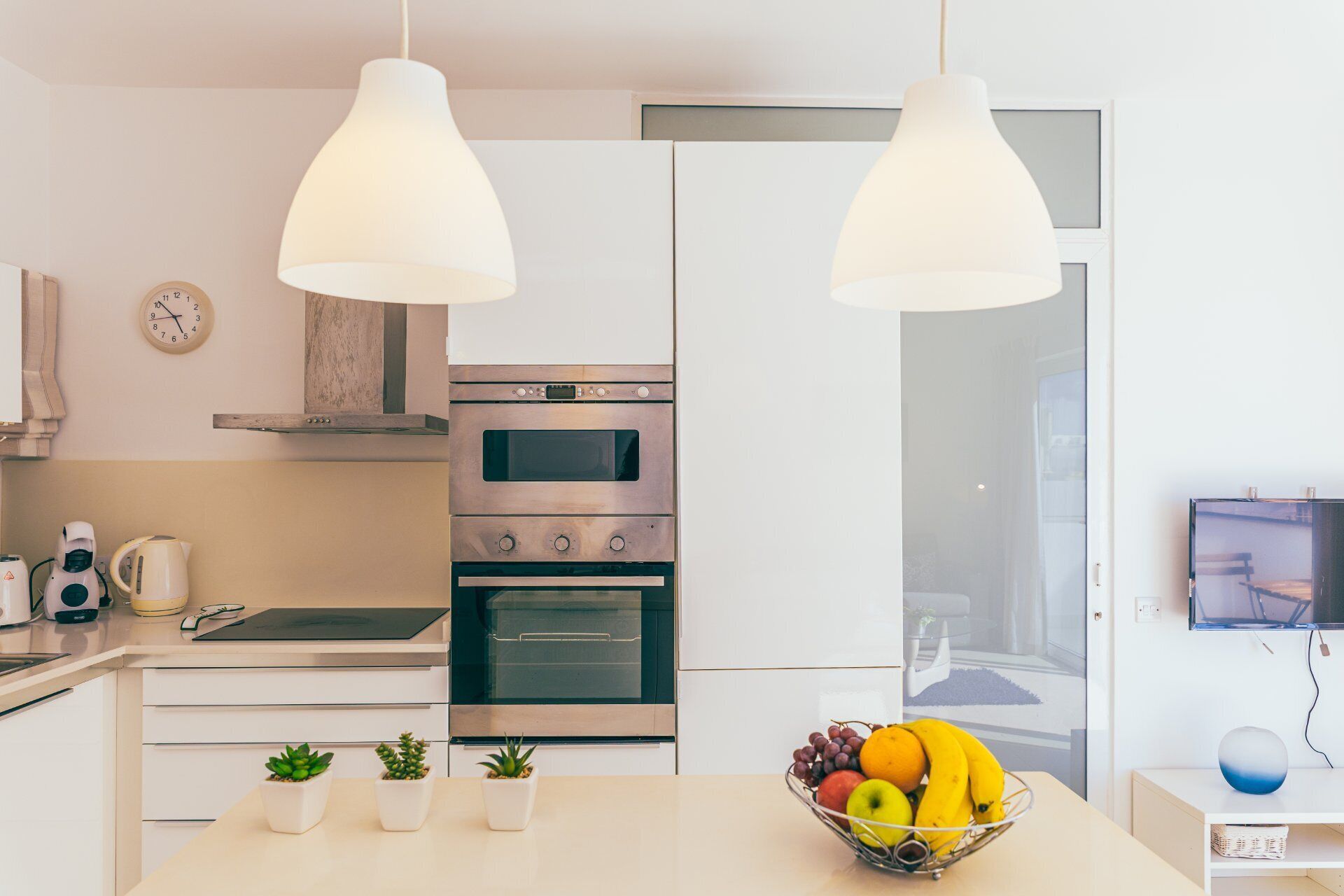 A modern kitchen with white cabinets, a built-in oven, a stove, and a fruit bowl on the counter.