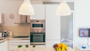 A modern kitchen with white cabinets, a built-in oven, a stove, and a fruit bowl on the counter.