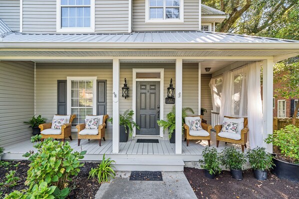 A house with a porch, two wicker chairs with cushions, a door, and potted plants. - Walk to Bay & Downtown Fairhope- Fig & Bay Retreat -Coastal Getaway with Pool! (Fairhope, AL)