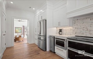 A modern kitchen with white cabinetry, stainless steel appliances, and a brick backsplash. - Walk to Bay & Downtown Fairhope- Fig & Bay Retreat -Coastal Getaway with Pool! (Fairhope, AL)