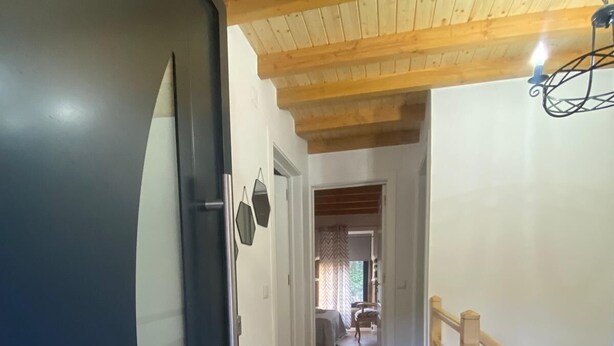 Käytävä, jossa on puulattia, tumma ovi ja puinen kaide, joka reunustaa portaita.