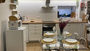 Moderni keittiö, jossa on ruokailutila. Tilan keskipisteenä on lasipöytä, jonka päällä on kultaiset alustat, sekä läpinäkyvät tuolit. Keittiössä on myös sisäänrakennettu uuni ja mikroaaltouuni.