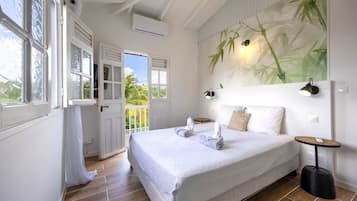 A bedroom with a bed, a nightstand, a wall-mounted lamp, and a view of the outdoors.