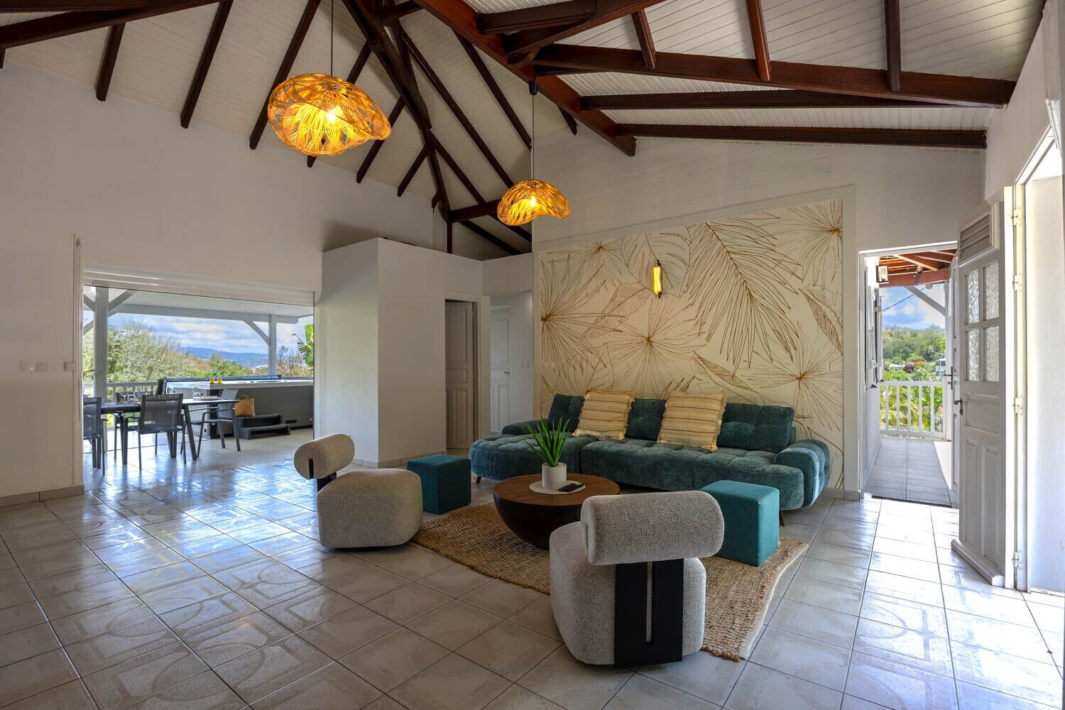 A spacious living room with a sofa, ottomans, and a coffee table. There is a large window and a view of the outdoors.