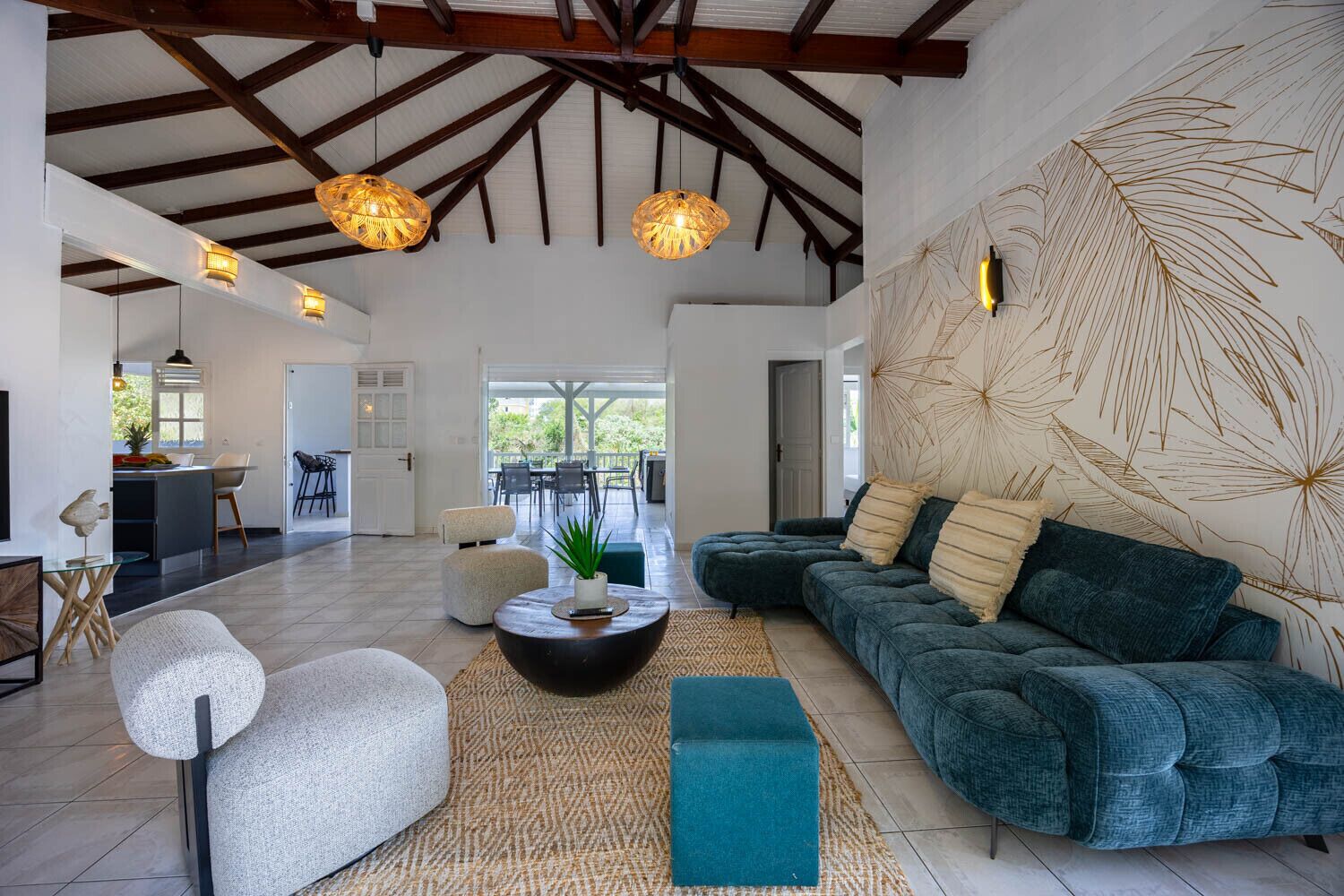 Un salon spacieux avec un plafond haut, un grand canapé, une table basse et un coin repas visible au fond.