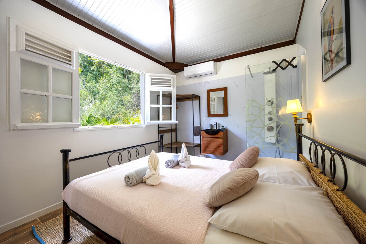 A bedroom with a bed, a bedside table, a mirror, a window, and a wall-mounted lamp.