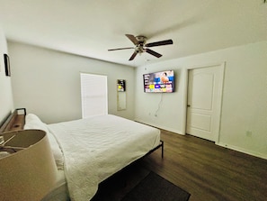 Una habitación de hotel con una cama, un ventilador de techo, un televisor montado en la pared y una puerta.