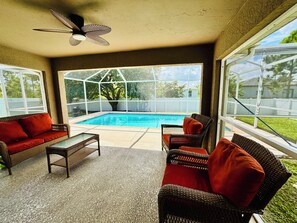 A covered patio area with a pool, wicker furniture, and a ceiling fan. - Salt water, screened-in heated pool house. 3 bed/2bath. (Lehigh Acres)