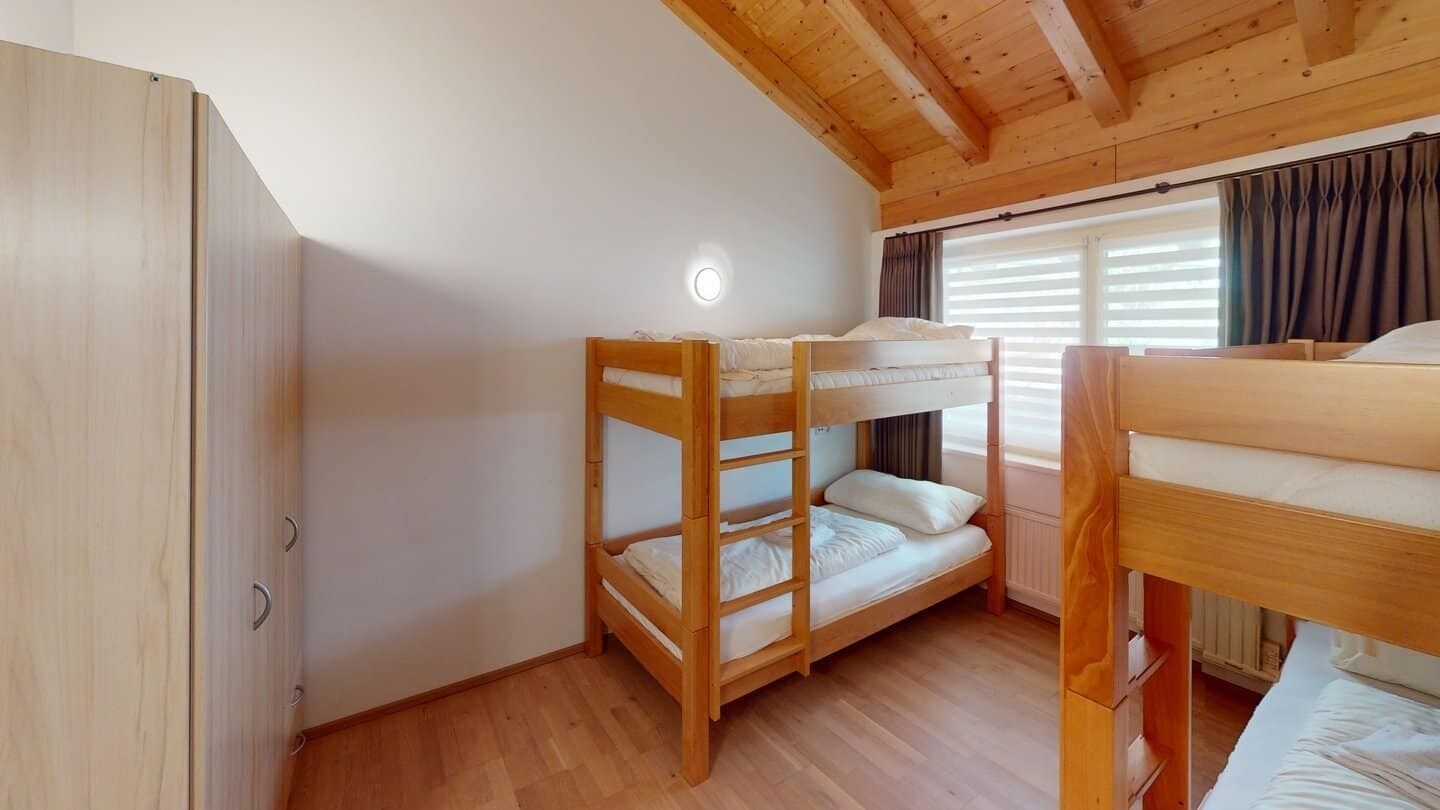 A bunk bed room with wooden walls and a ceiling, a wardrobe, and a window with curtains.