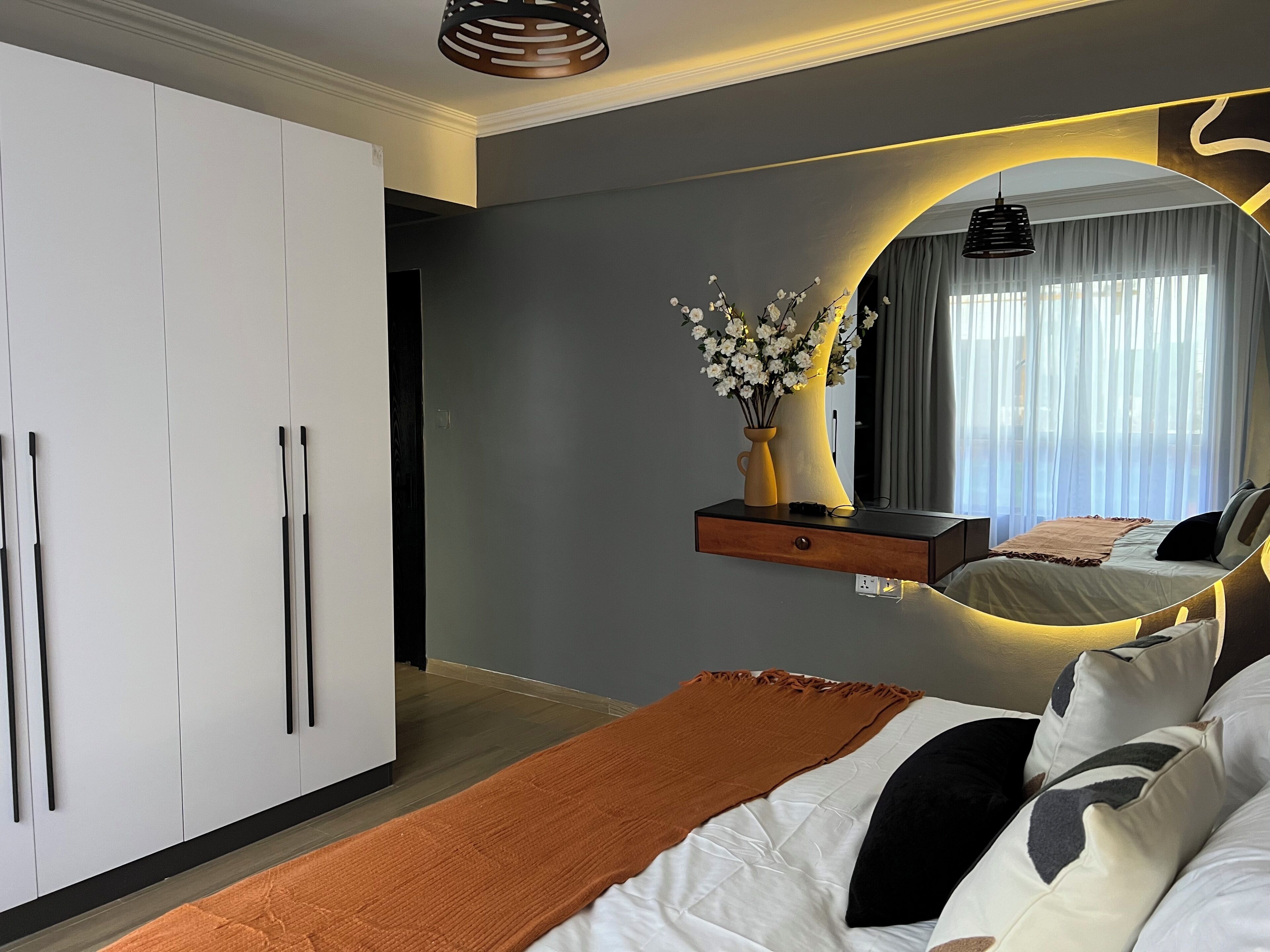 Une chambre à coucher avec un lit, une armoire, un miroir et un vase de fleurs.