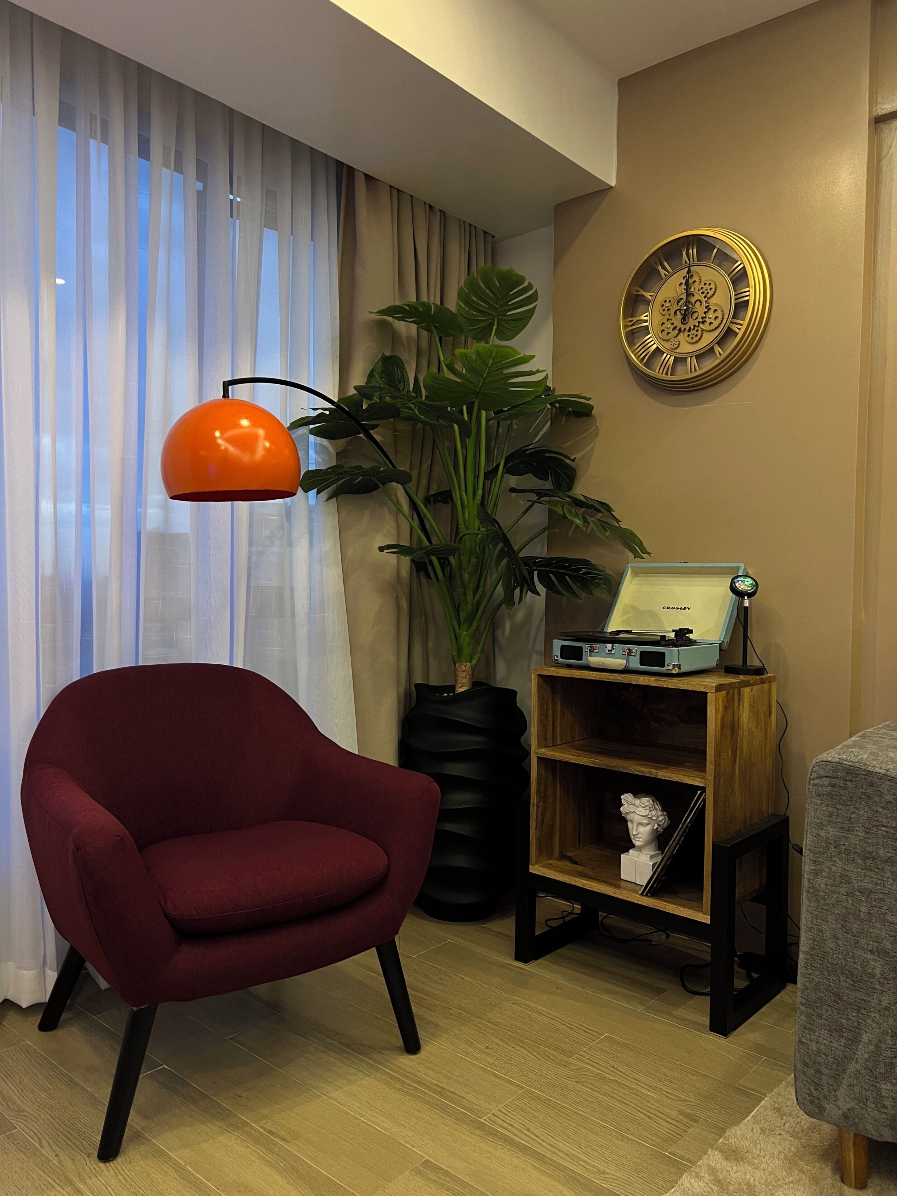 A room with a red armchair, a plant, a clock, and a vintage record player.