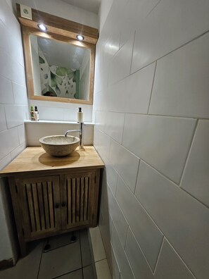 A bathroom with a wooden vanity, a large basin, a mirror, and white tiled walls.
