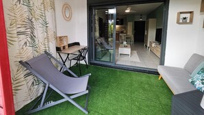 Ein Zimmer mit einer Schiebetür aus Glas, die zu einer Küche führt, mit grauem Lounge-Sessel, weißem Sofa und Deckenventilator.