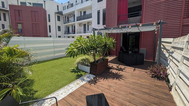 Eine Dachterrasse mit Gartenmöbeln, ein kleiner Gartenbereich mit Pflanzen und Blick auf angrenzende Gebäude.