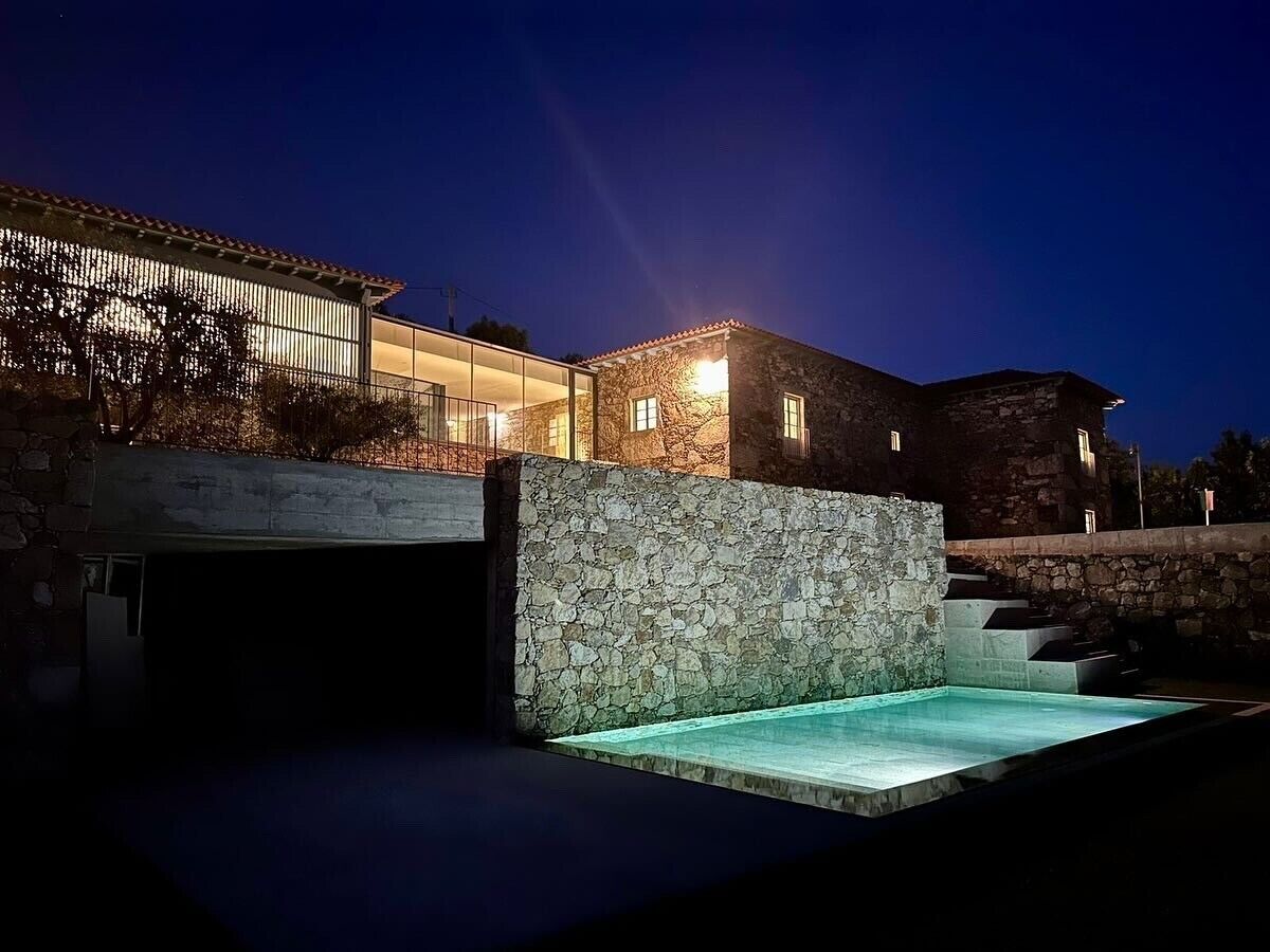 A modern building with a stone facade, a swimming pool, and a covered area with glass walls.