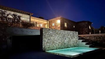 A modern building with a stone facade, a swimming pool, and a covered area with glass walls.