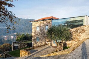 A stone building with a glass extension, a stone staircase, and a view of a valley. - Capim Limão Country House (Ponte de Lima)
