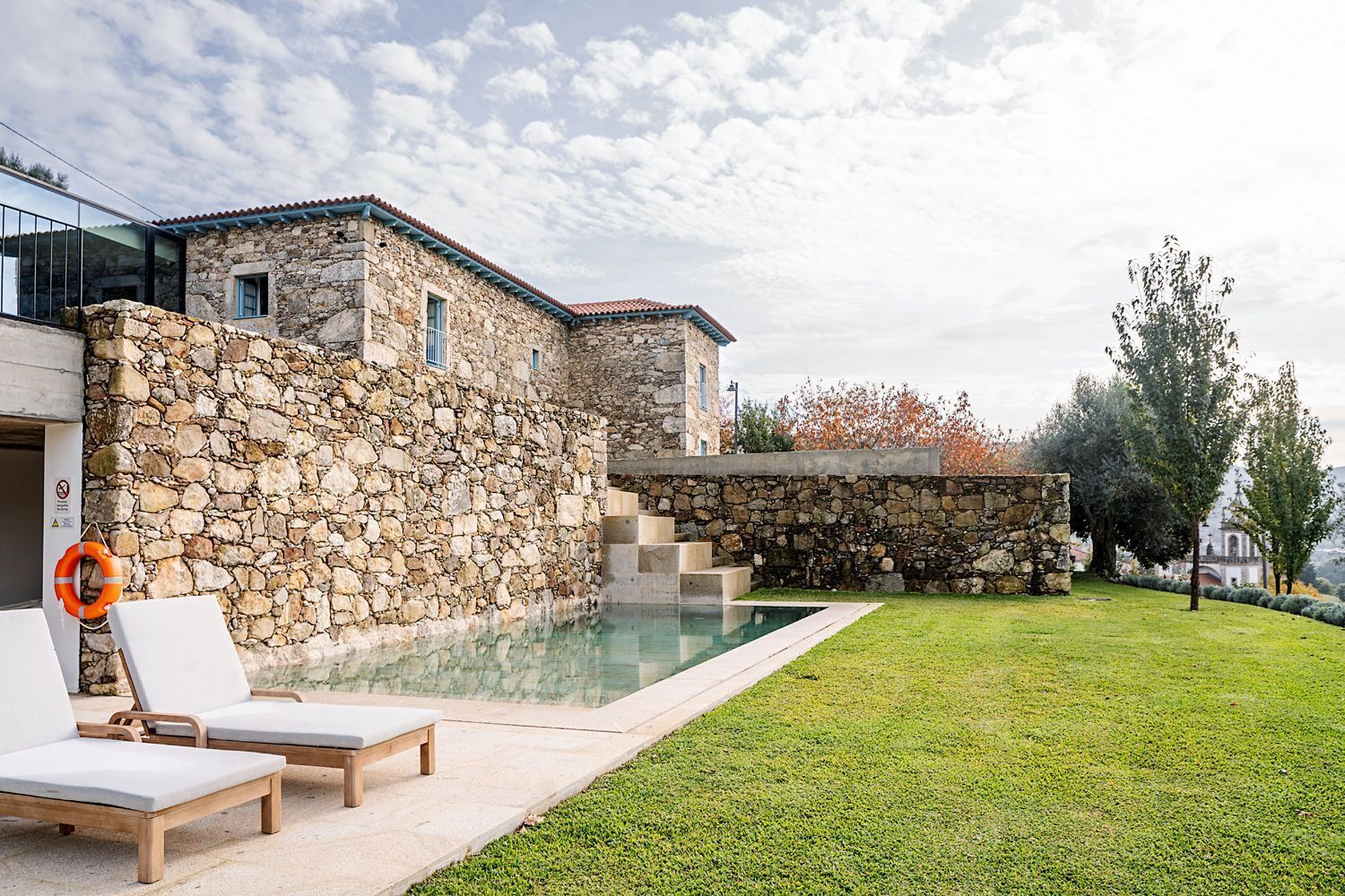 A stone building with a swimming pool, outdoor seating, and a grassy area.