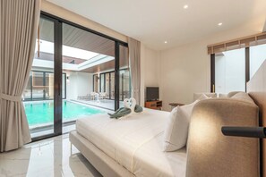 A modern hotel room with a large bed, a TV, and a view of an outdoor swimming pool. - New Pool Villa With Fitness and Tennis Court (Thep Krasattri)