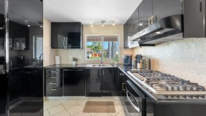 A modern kitchen with black cabinets, a stainless steel range, and a window with a view. - Resort-Style Pool Retreat | Home Gym + Hot Tub (Goleta)