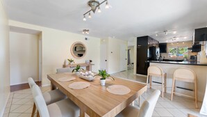 A modern kitchen with a central island, a dining area with a wooden table and chairs, and a living area with a TV and seating. - Resort-Style Pool Retreat | Home Gym + Hot Tub (Goleta)