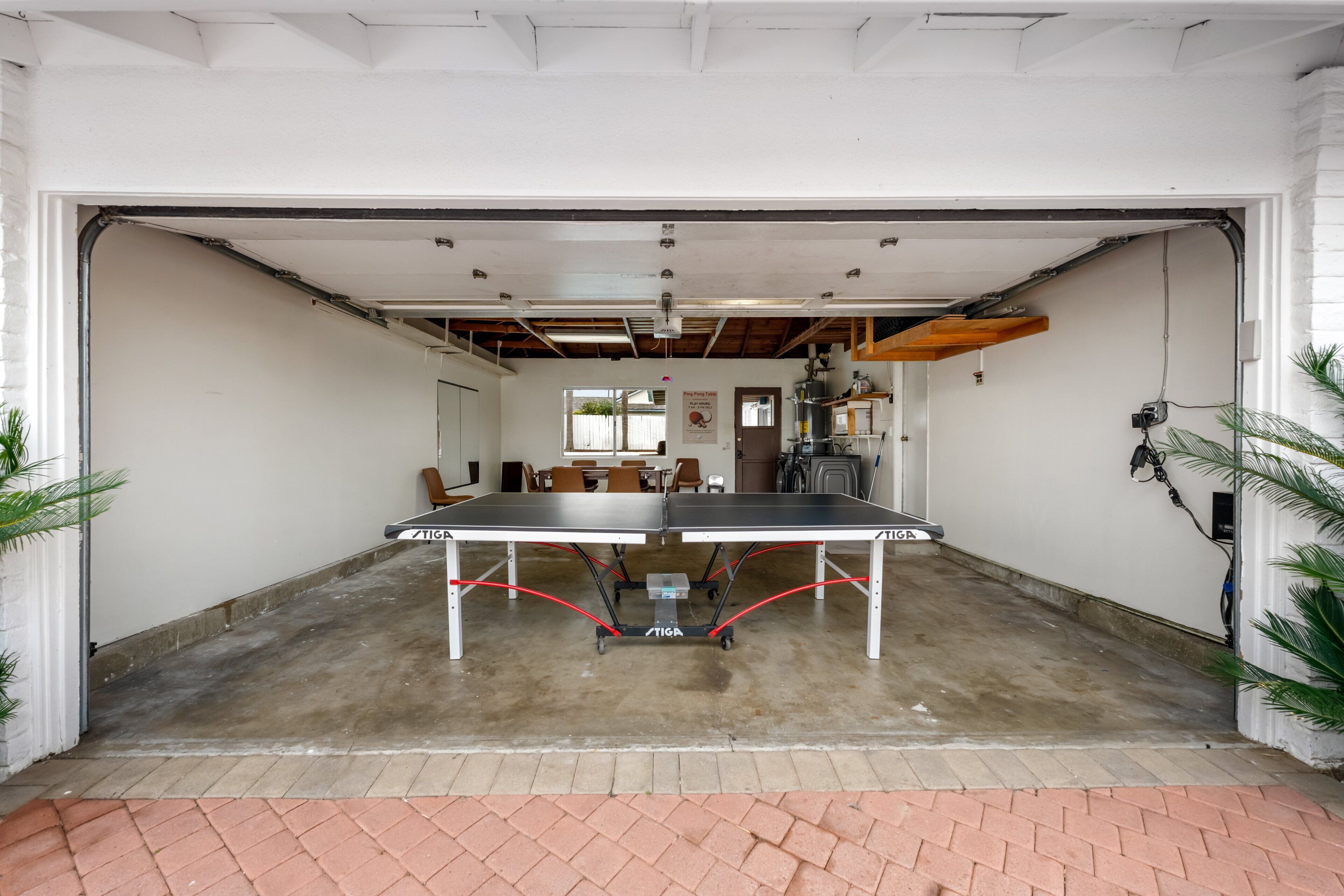 Un vaste espace intérieur comprenant une table de ping-pong, un sol en béton et un chemin en briques menant à un garage.