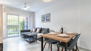 Una sala de estar moderna con un sofá, una mesa de comedor para cuatro comensales y un ventilador de techo.
