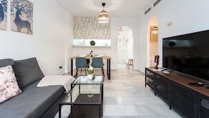 Una sala de estar moderna con un sofá, una mesa de centro, televisión y un comedor con sillas y una mesa.