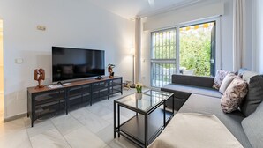 Una sala de estar moderna con un televisor de pantalla plana, una mesa de centro de vidrio, un sofá y un ventanal con vistas a zonas verdes.