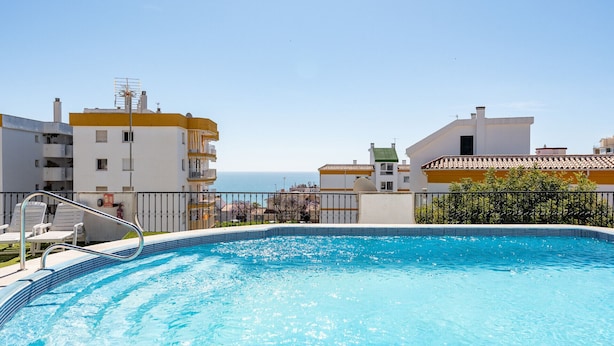 Una piscina con vista al mar, rodeada de edificios con balcones.