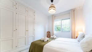 Un dormitorio con cama, una silla, un ventanal y un armario.