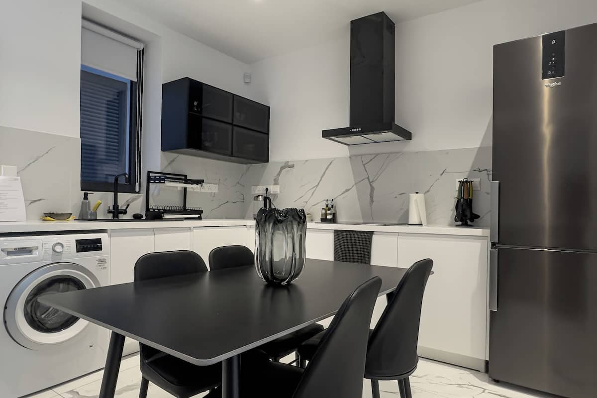 Una cocina moderna con lavadora integrada, una mesa de comedor con sillas, una campana extractora negra y un refrigerador de acero inoxidable.